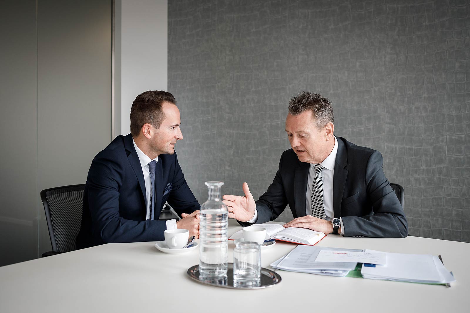 Doktor Lassingleithner und Doktor Egger im Gespräch, sitzend an einem Tisch.